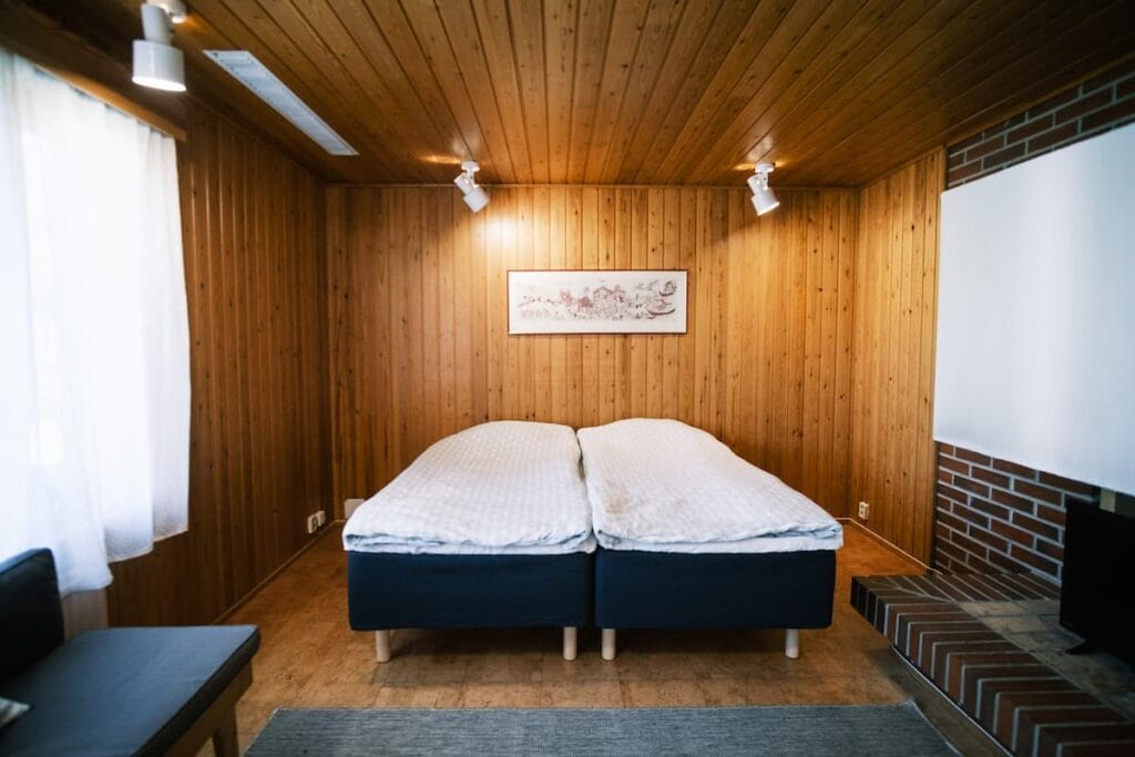 Ett sovrum med två enkelsängar placerade bredvid varandra, väggar och tak klädda med träpaneler samt en tegelstenad öppen spis till höger.