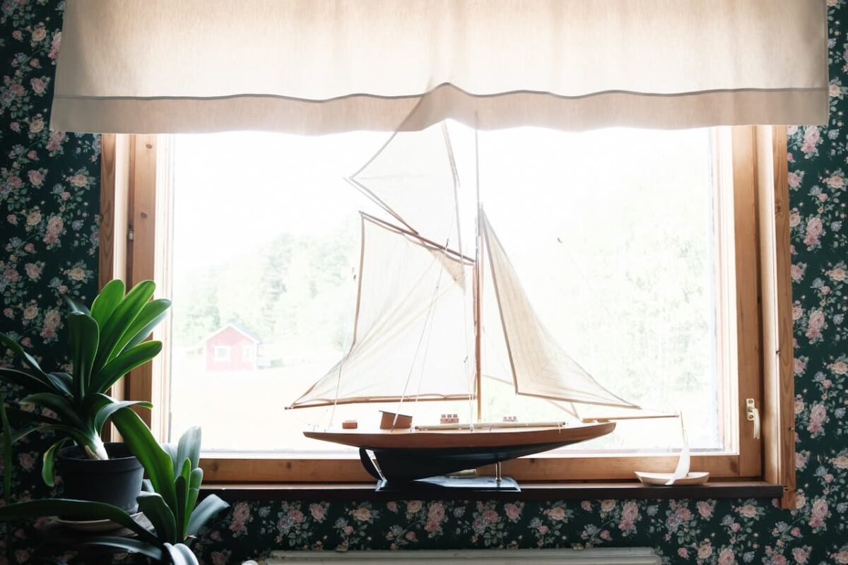 Modell segelbåt på en fönsterbräda med utsikt över landskapet.