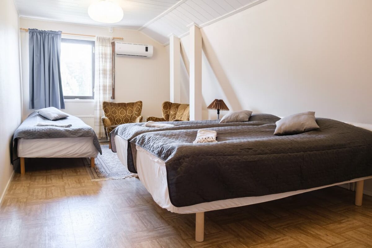 Ett snyggt arrangerat sovrum med två sängar, den ena större än den andra, med parkettgolv, luftkonditionering och enkel inredning.