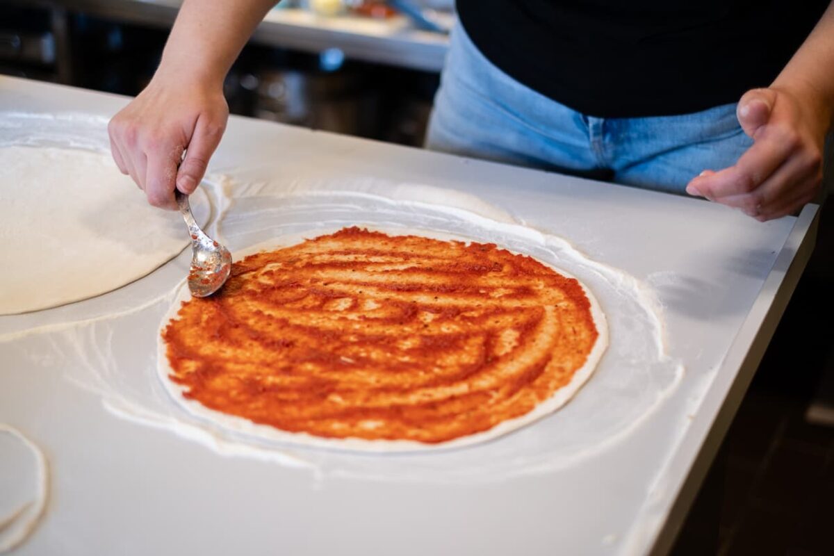 Person spreading tomato sauce on pizza dough.