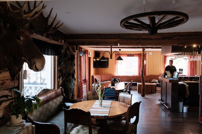 Mysig interiör i en rustik restaurang i stugstil med trämöbler och ett älghuvud på väggen.