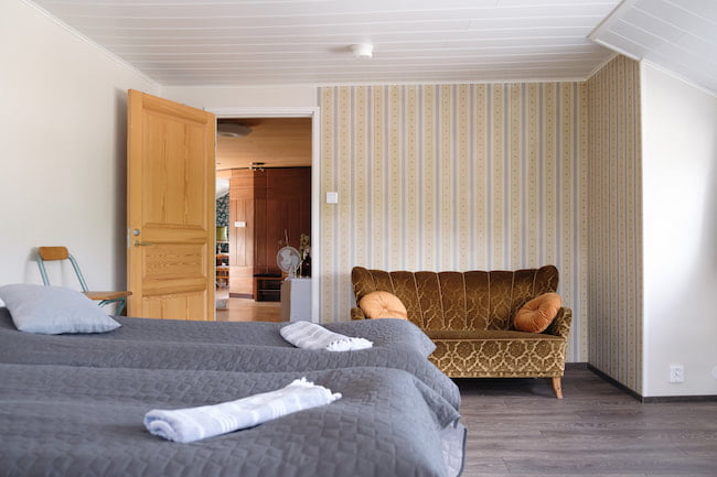 Ett mysigt hotellrum med mönstrad soffa, snyggt bäddad säng och en öppen dörr som leder till ett annat rum.