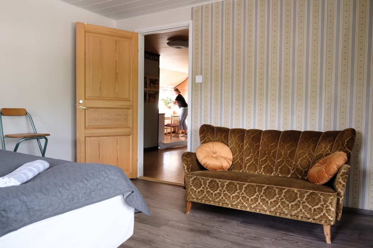 Ett sovrum i vintagestil med mönstrad tapet, trädörr, brun soffa och en säng med blått överdrag.