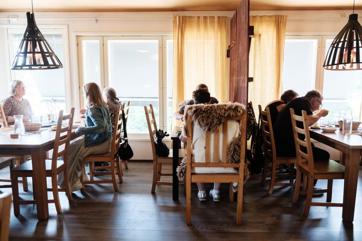 Gäster som äter vid träbord i en mysig, väl upplyst restaurang.