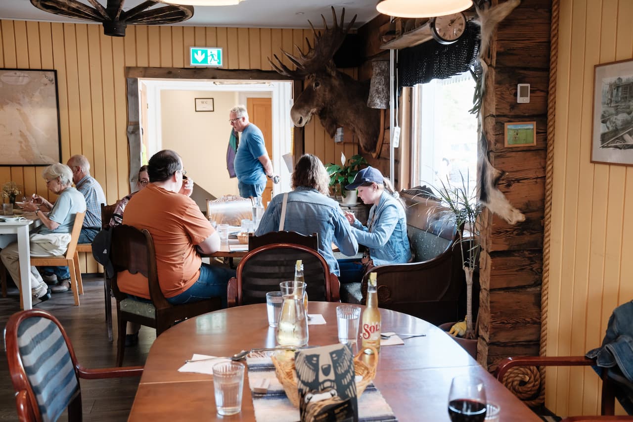 Gäster som äter på en rustik restaurang med ett älghuvud monterat på väggen.