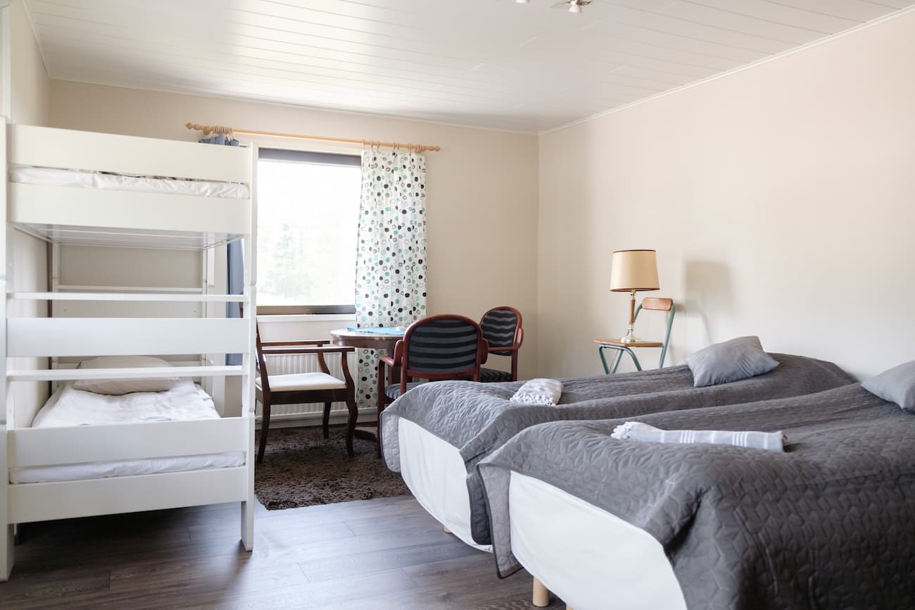 Ett snyggt sovrum med två enkelsängar och en våningssäng samt ett litet skrivbord och en stol nära ett fönster med gardiner.